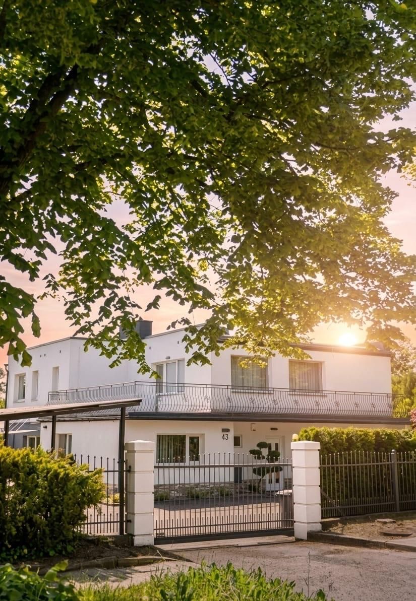 Weißes Haus Nr. 43 hinter dem Einfahrtstor, im Schatten eines großen Baums in der Abendsonne