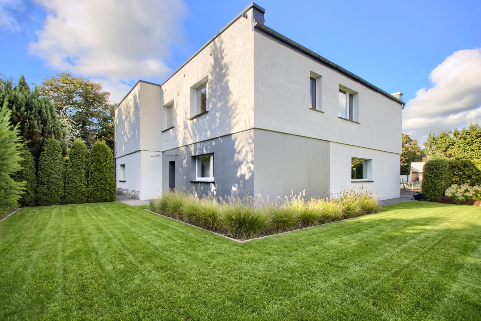 Weißes zweigeschossiges Haus mit Flachdach, Gartenansicht mit Rasen und Ziergräsern