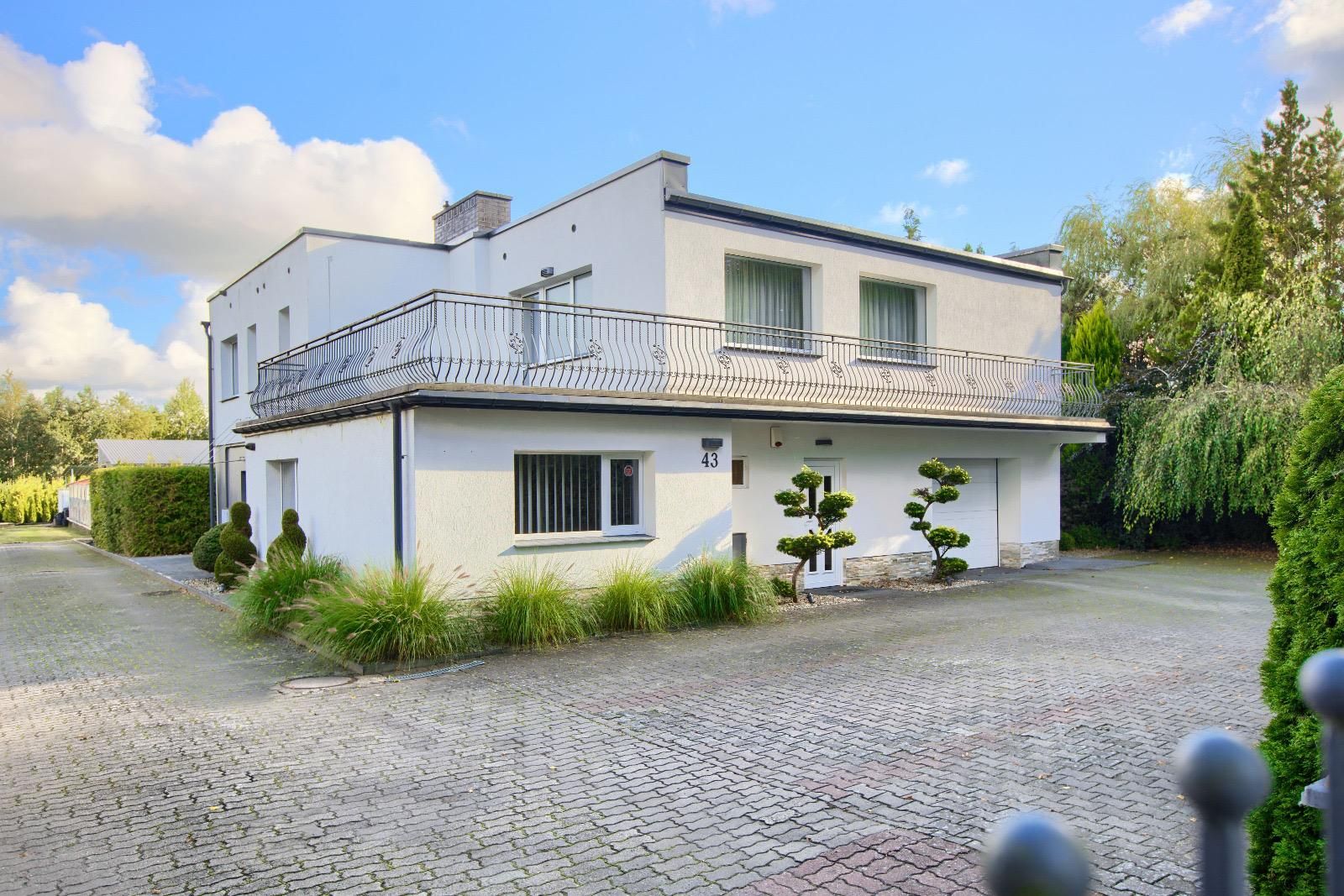 Hausfront mit langem Balkon mit schmiedeeisernem Geländer und gepflasterter Einfahrt