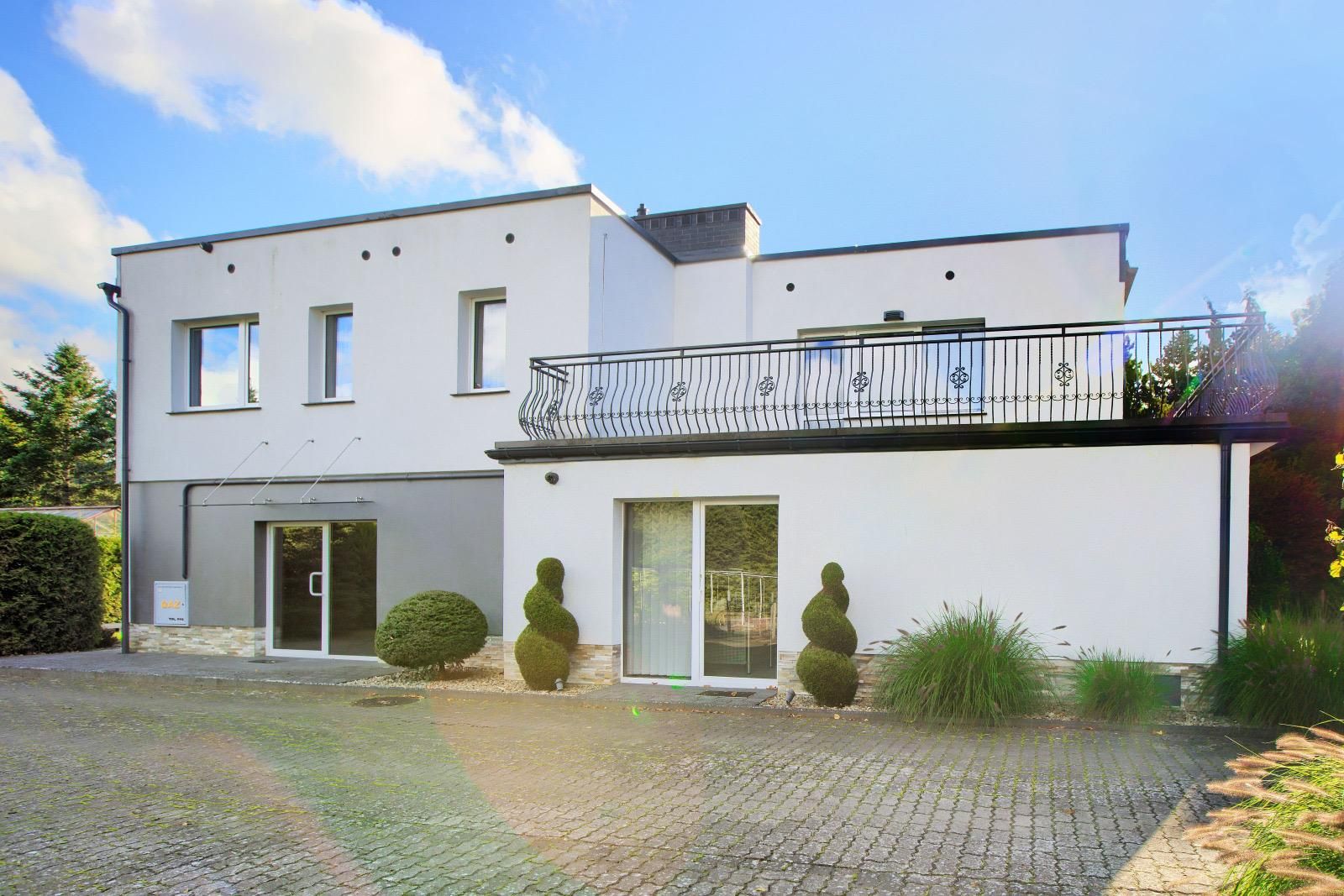 Fassade mit Terrasse über dem Erdgeschoss, Glastüren und Formgehölzen
